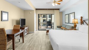 Ein Hotelzimmer mit Bett, Fernseher, Esstisch mit Stühlen, Deckenventilator und einem Balkon mit Aussicht.