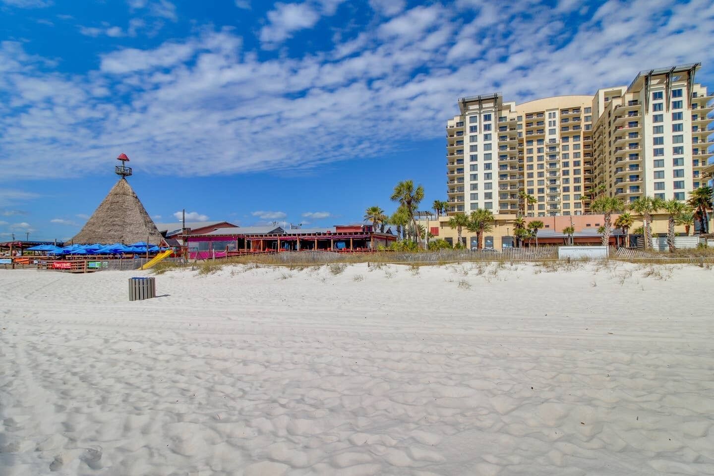 Un hotel sulla spiaggia con un edificio grande, un'area ombrelloni e una torretta per i bagnini.