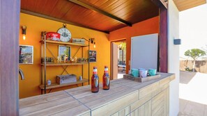 Zona de bar con estantes llenos de botellas y vasos, un reloj y una bandeja de tazas.