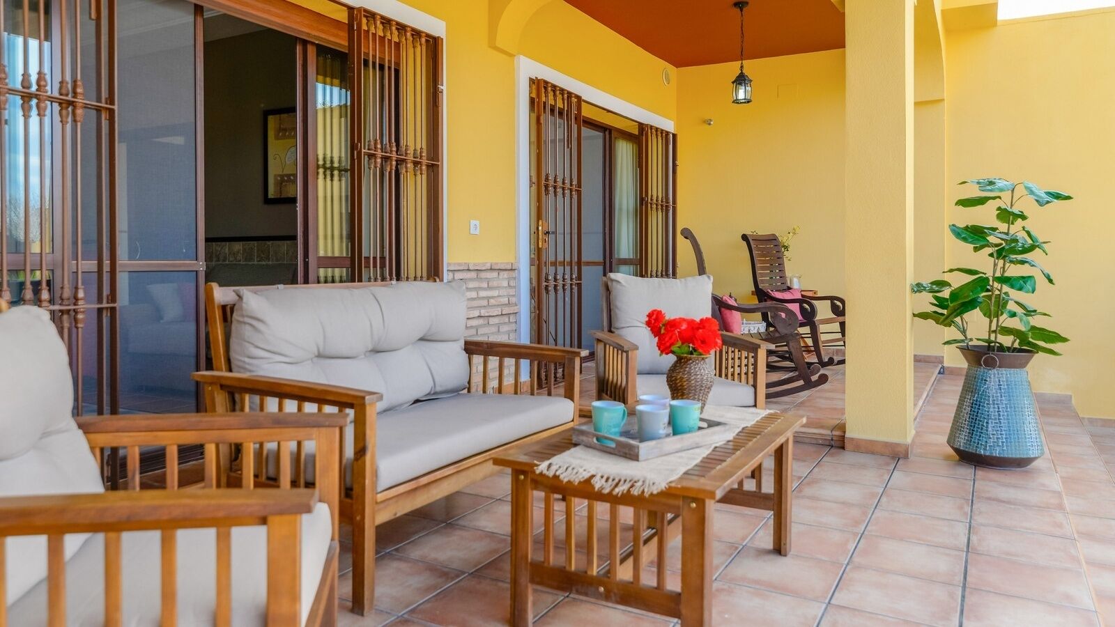 Un patio acogedor con mobiliario de madera, incluyendo un sofá y sillas, una mesita con una bandeja de objetos, y una planta en maceta.