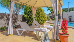 Un espacio al aire libre techado con sillones de descanso y una piscina.