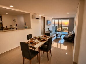 A modern dining area with a table set for four, a kitchen with a built-in oven, and a balcony with a view of the sunset.