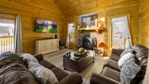 L’intérieur d’un chalet en bois chaleureux et accueillant, avec une cheminée, des sièges confortables et un téléviseur.