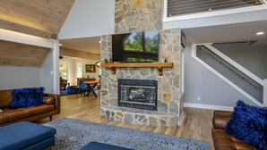 Un salon moderne avec une cheminée en pierre, un téléviseur fixé au-dessus et un escalier menant à l’étage supérieur.