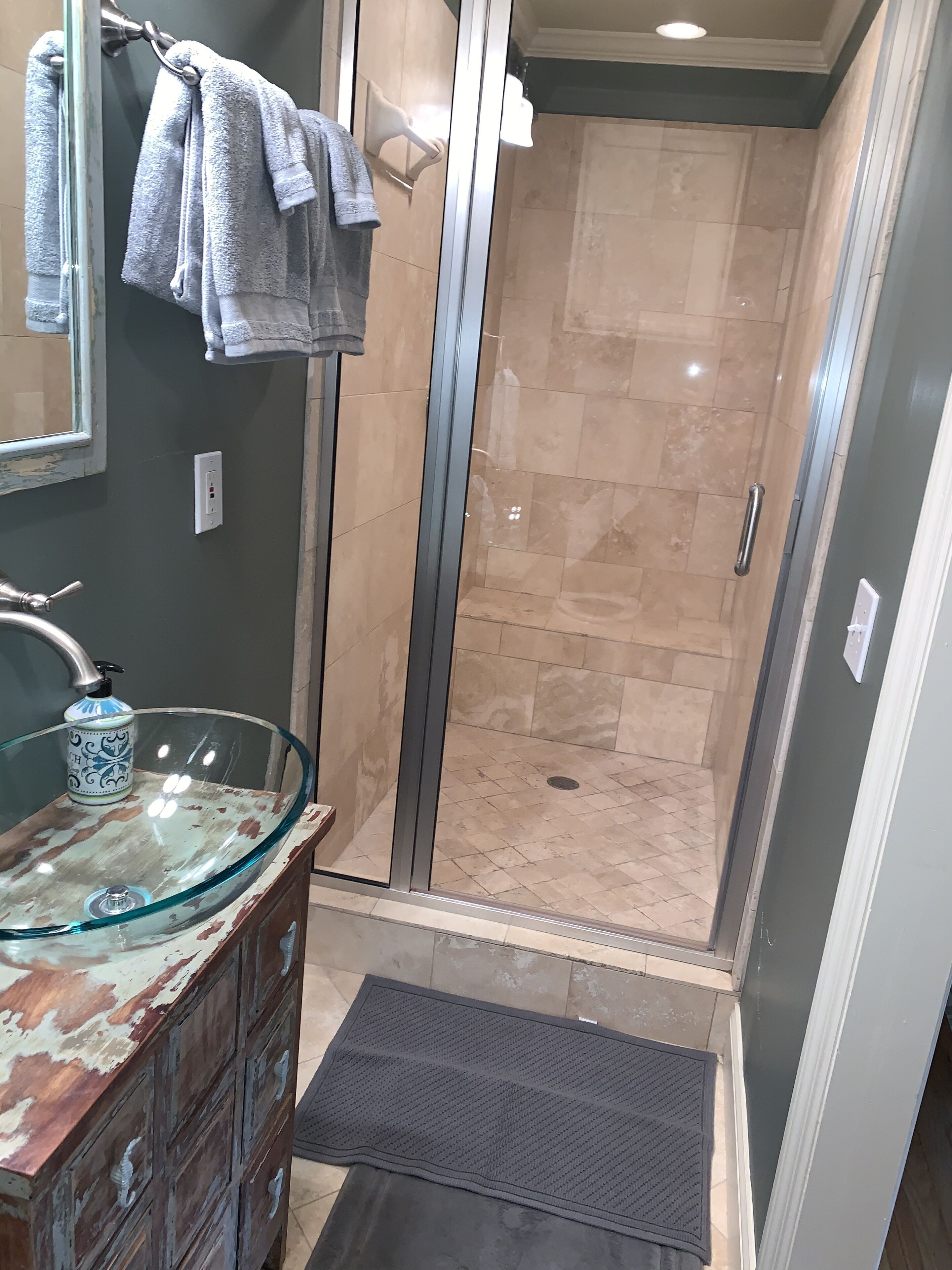 Un baño con lavamanos de vidrio, ducha con puerta de vidrio y un toallero con varias toallas.