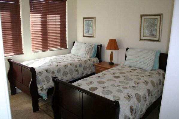 A bedroom with two single beds, a nightstand, a lamp, and two framed pictures on the wall.