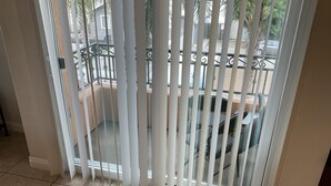 A room with a balcony featuring white blinds, a tiled floor, and a view of a parked car and greenery outside. - Carlsbad Village, Great Beach Access, Shops & Restaurants (Carlsbad)