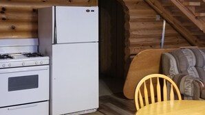 L’intérieur d’une cabane en bois comprend un espace cuisine équipé d’un poêle, d’un réfrigérateur et d’un plafond en bois.