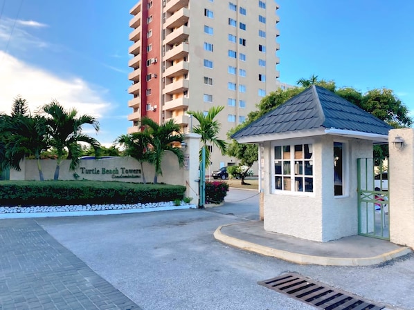 A gated entrance to Turtle Beach Towers with a small kiosk and a paved area with a drainage grate.