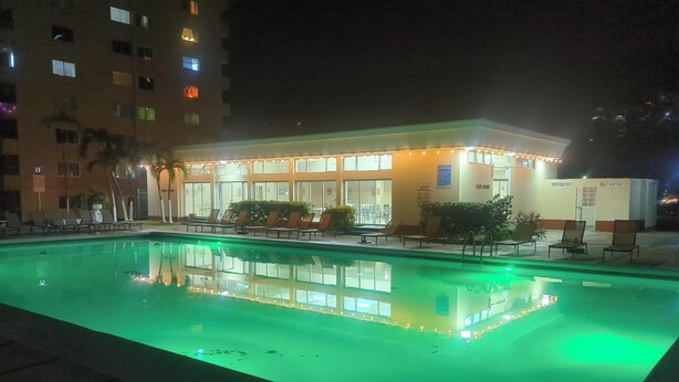 A hotel with a swimming pool, lounge chairs, and a well-lit building facade.