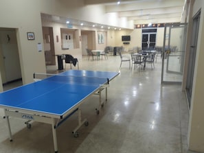 A spacious room with a ping pong table, multiple chairs, and tables, likely a recreational area.