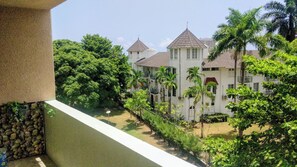 A white building with multiple windows and a red roof, surrounded by lush greenery and palm trees.
