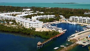 An aerial view of a coastal hotel with multiple buildings, a marina with boats, and a pier extending into the water.
