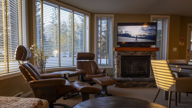 A living room with a fireplace, leather chairs, a television, and a stone fireplace surround. - On ski resort mountain 2 bedroom 2 bathroom condo, access to hot tub and sauna (Fernie)