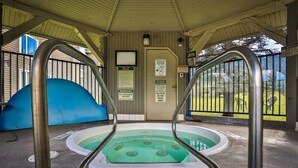 A covered swimming pool area with metal railings, a door with a warning sign, and a view of the outdoors. - On ski resort mountain 2 bedroom 2 bathroom condo, access to hot tub and sauna (Fernie)