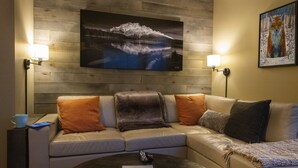 A living room with a sofa, two wall-mounted lamps, a painting of a mountain, and a framed artwork of a fox. - On ski resort mountain 2 bedroom 2 bathroom condo, access to hot tub and sauna (Fernie)