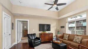 Un salon spacieux doté d’un ventilateur de plafond, d’un téléviseur à écran plat, d’un canapé marron, d’un fauteuil en cuir noir et d’un meuble en bois.