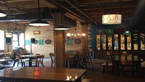 L’intérieur d’un restaurant est aménagé avec des tables et des chaises en bois, des suspensions décoratives et un coin bar doté d’étagères.