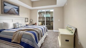 A bedroom with a bed, a desk, a chair, a dresser, and a sliding glass door to a balcony. - Gorgeous Condo in the heart of Grand Haven (Grand Haven)