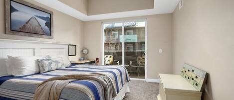 A bedroom with a bed, a desk, a chair, a dresser, and a sliding glass door to a balcony.