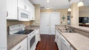Une cuisine avec des meubles blancs, une cuisinière, un four, un four à micro-ondes, un évier et un lave-vaisselle.