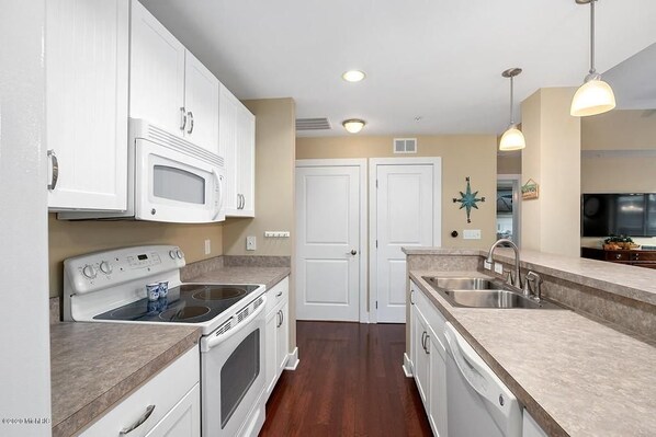 A kitchen with white cabinets, a stove, an oven, a microwave, a sink, and a dishwasher.