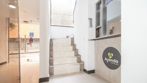 A hotel reception area with a staircase leading to an upper floor, a reception desk with the hotel's logo, and a glass door entrance. - Ayenda 1086 Torre 52 (Bogotá)