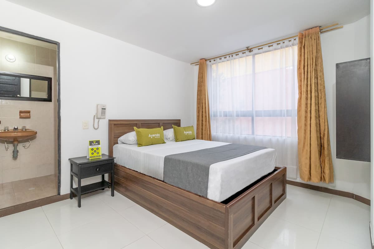 A hotel room with a wooden bed, a bedside table with a phone, a small sink, and a window with curtains.