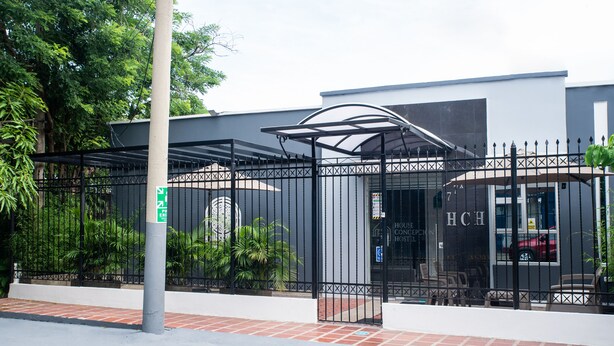 Un edificio moderno con entrada protegida por un portón, un área de estar al aire libre techada y un cartel que indica un lugar de culto.
