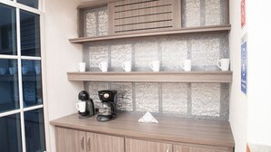 Una cocina con armarios de madera, una cafetera y tazas blancas en estantes.