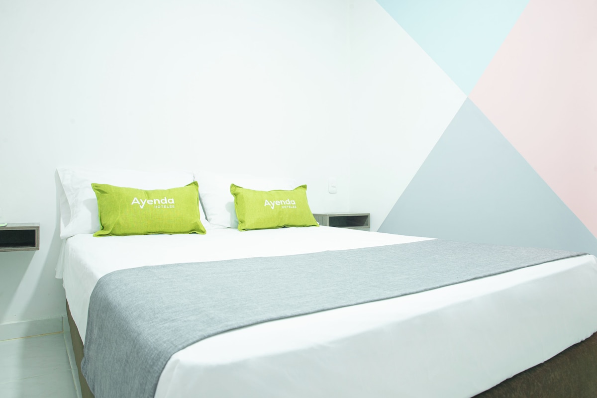 A bed with two green pillows labeled "Ayenda Hotels" and a gray blanket.
