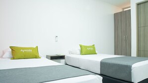 Habitación de hotel con dos camas, cada una con cubrecama gris y almohada verde con el texto 