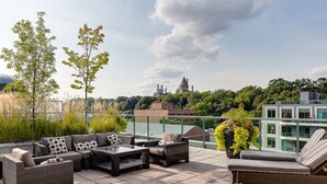 Una terraza en la azotea con mobiliario de mimbre, una mesa de vidrio y una vista de un edificio que parece castillo al fondo.