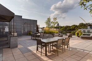 Une terrasse extérieure avec des tables et des chaises, un grand bac à fleurs et, en arrière-plan, une vue sur un château.