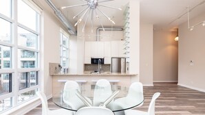 Una cocina moderna con una isla central, electrodomésticos de acero inoxidable y una mesa de comedor de vidrio con sillas blancas.