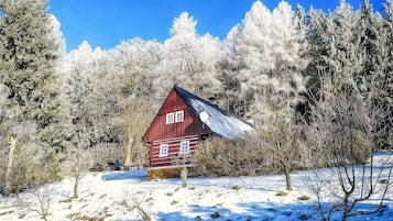 A red wooden cabin surrounded by snow-covered trees.
