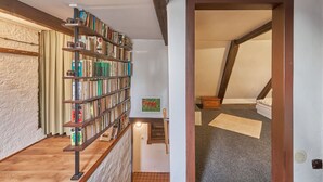 Un intérieur à plusieurs niveaux, avec un escalier en bois, une bibliothèque remplie de livres et une petite table agrémentée d’un objet décoratif.