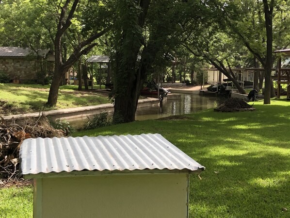 A small, single-story building with a corrugated metal roof, surrounded by lush green grass and trees. - A Cozy, quiet and most perfect cottage beautifully located on a waterfront cove. (BURNET)