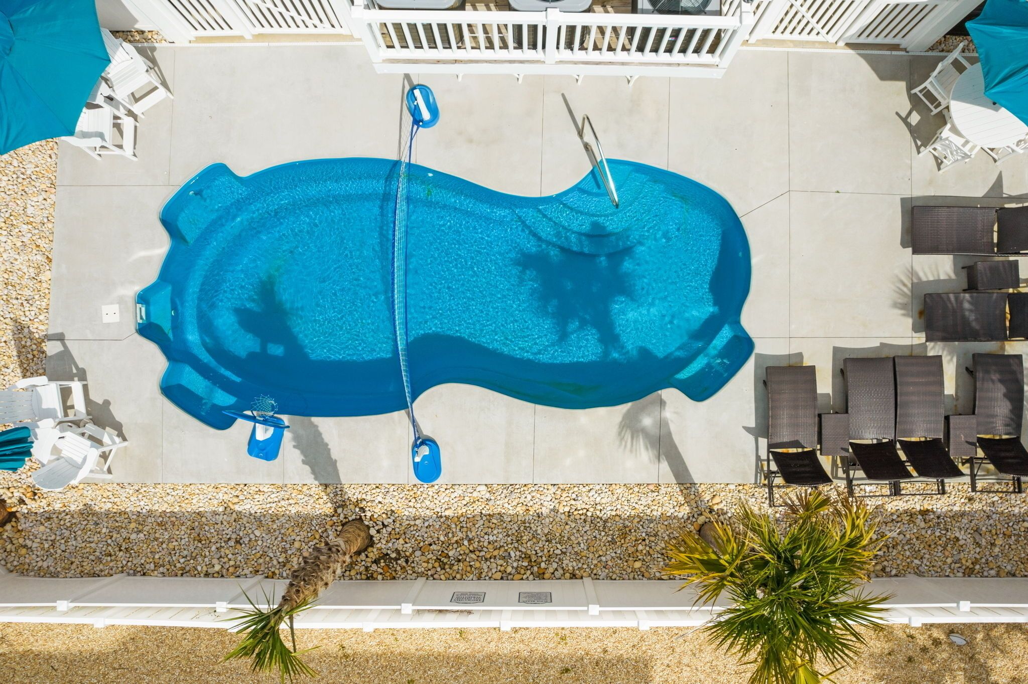 An aerial view of a swimming pool with a diving board, surrounded by lounge chairs and a pebble-lined walkway.