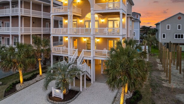 Ein mehrstöckiges Strandhotel mit Balkonen, Außenbeleuchtung und Palmen.