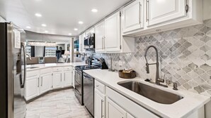A modern kitchen with white cabinetry, a stainless steel refrigerator, a double sink, and a patterned backsplash. - Inlet Reef 518-Beachfront Complex without Beachfront Prices! (Destin)
