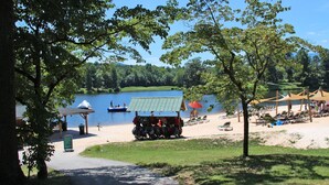 A lakeside park with a boat dock, picnic tables, and a sandy beach area with umbrellas and lounge chairs. - Eagles Court Ski In/Ski Out Condo with Walkable Location & Mountain Views! (Wintergreen Resort)