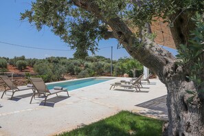 A swimming pool with lounge chairs, a tree, and a view of the surrounding landscape.