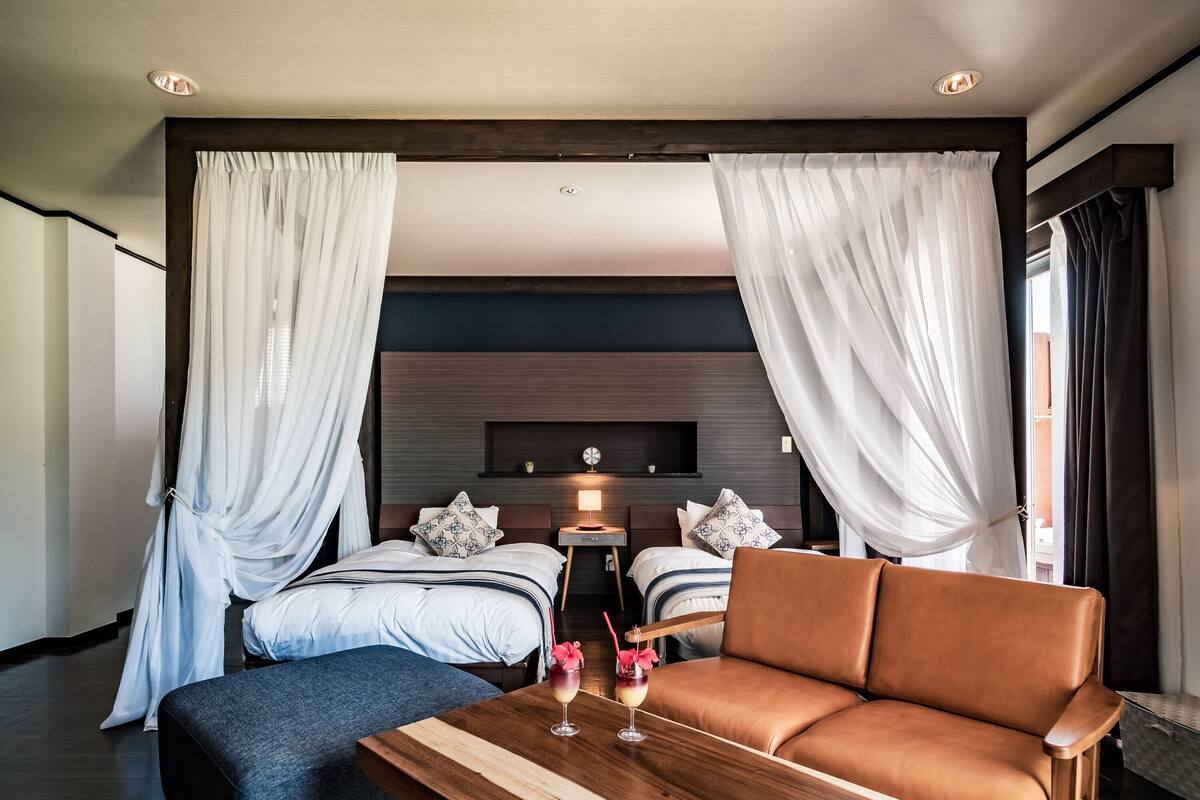 A modern hotel room with a large bed, a sofa, a wooden coffee table, and a TV mounted on the wall.