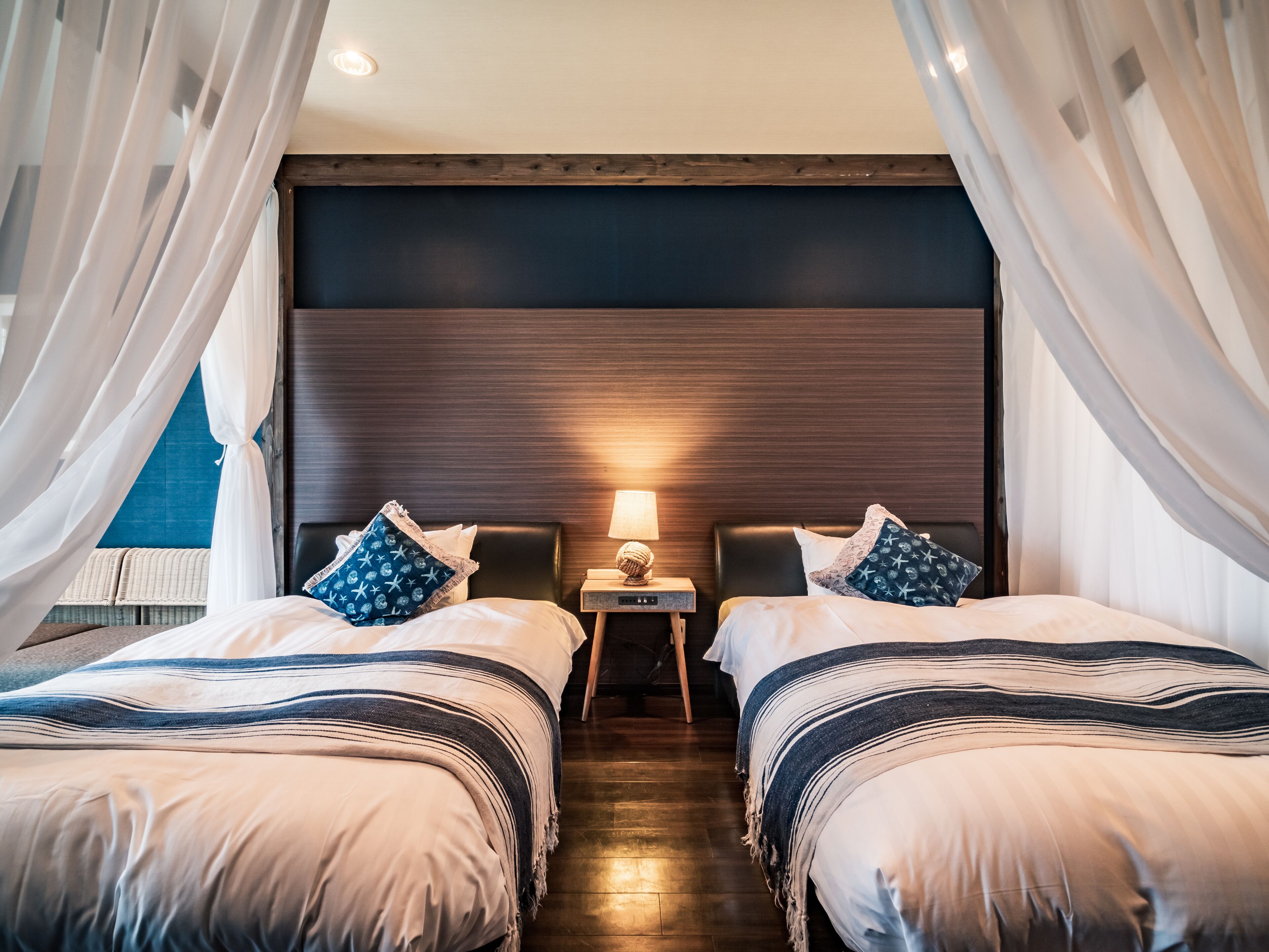 A hotel room with two beds, a nightstand with a lamp, and a view of the outside.