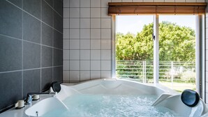 A modern bathroom with a large bathtub, tiled walls, and a view of greenery outside.