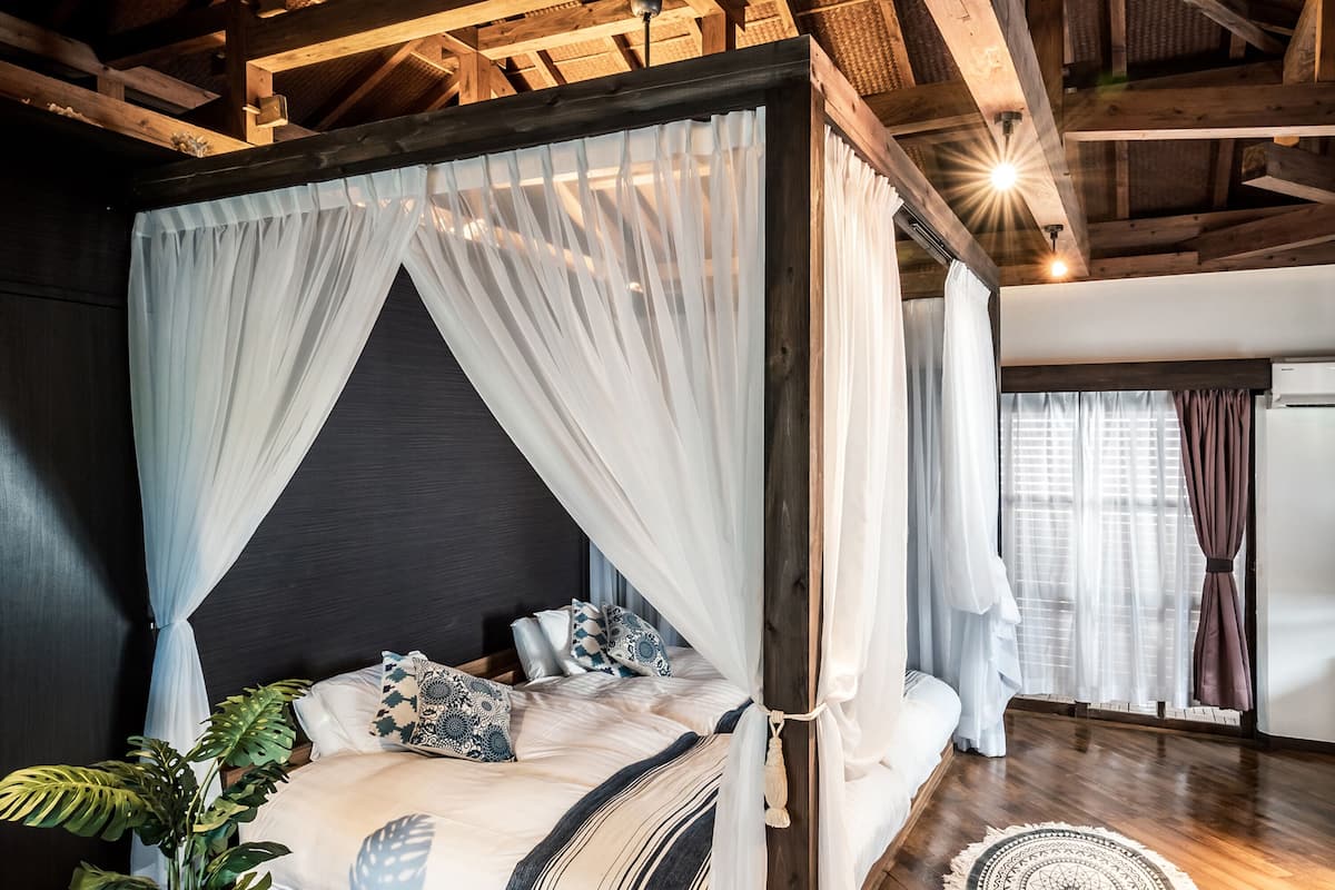 A four-poster bed with sheer curtains, a dark headboard, and patterned pillows.