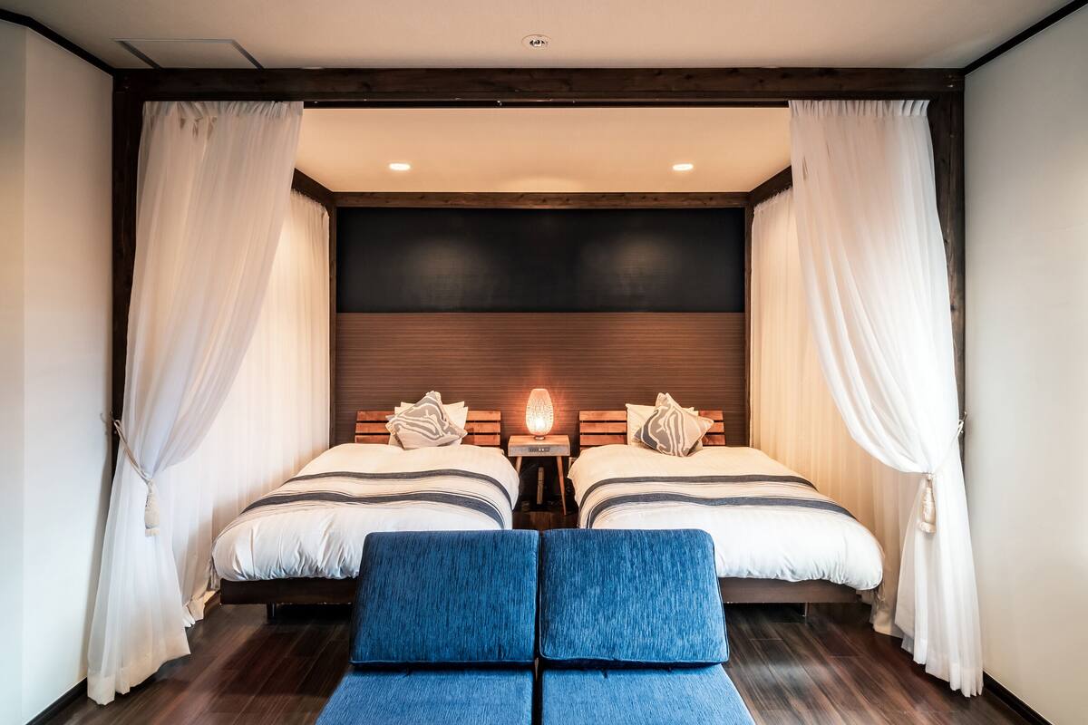 A double room with two beds, a wooden headboard, a small table with a lamp, and a blue bench.
