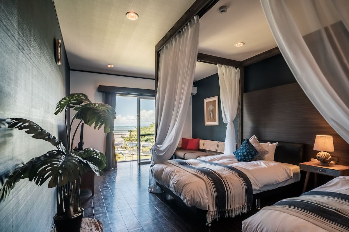 A modern bedroom with a large window, a potted plant, and a bed with a striped blanket.