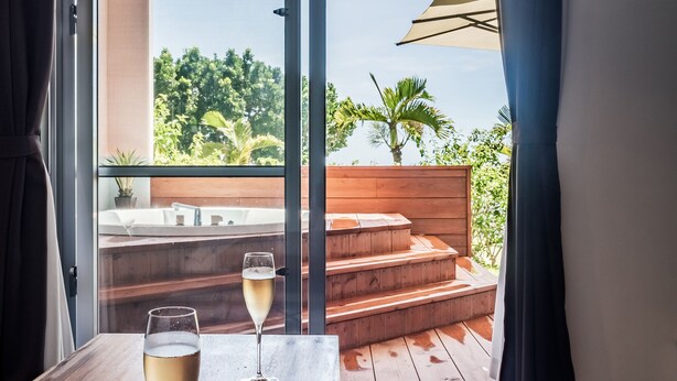 A room with a wooden table, two glasses of champagne, and a view of a wooden deck and outdoor area.